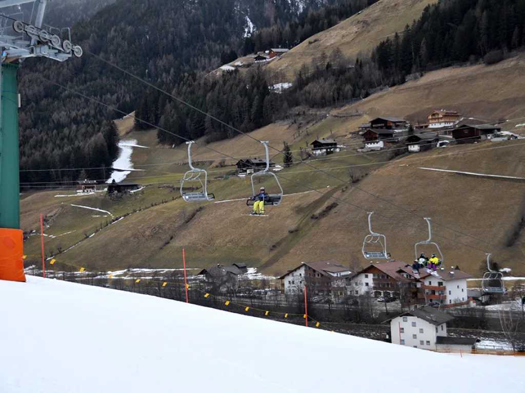 Blick vom Pistenrand auf das Dorf und die aperen Wiesen im Tal.